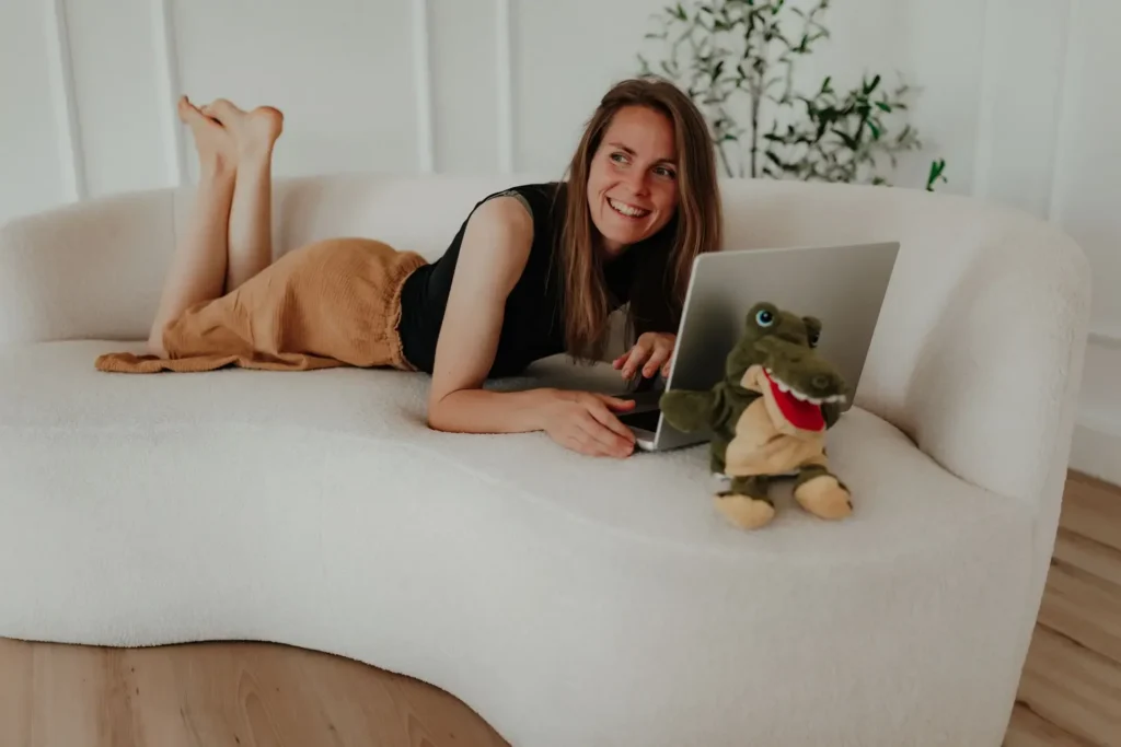 Linda liegt lachend mit Laptop auf dem Sofa